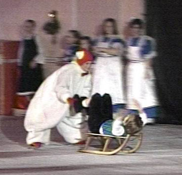 A rat pushing a sled that has a doll on it.  The doll is lying on her back on the sled with her legs and arms in the air